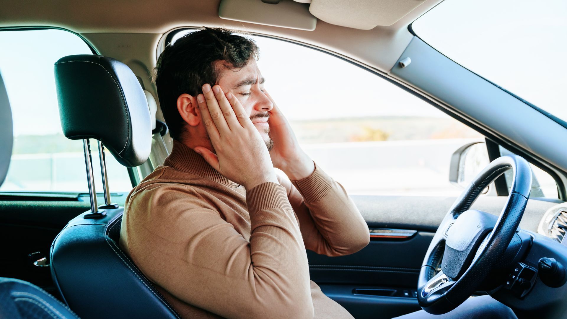 Man sitting in a car with hands on his face, looking stressed or overwhelmed while driving