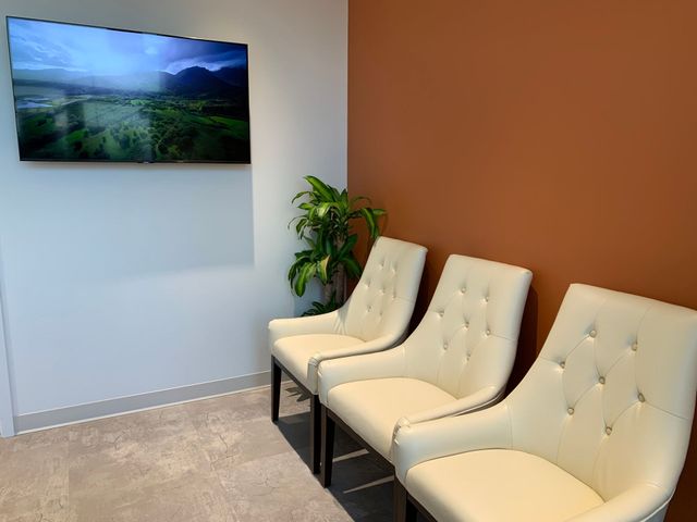 Modern waiting area with wall-mounted TV, beige chairs, a plant, and a brown accent wall