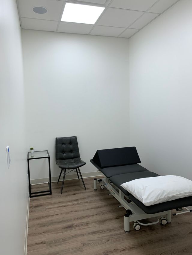 Exam room with exam table, chair, and small side table against white walls.