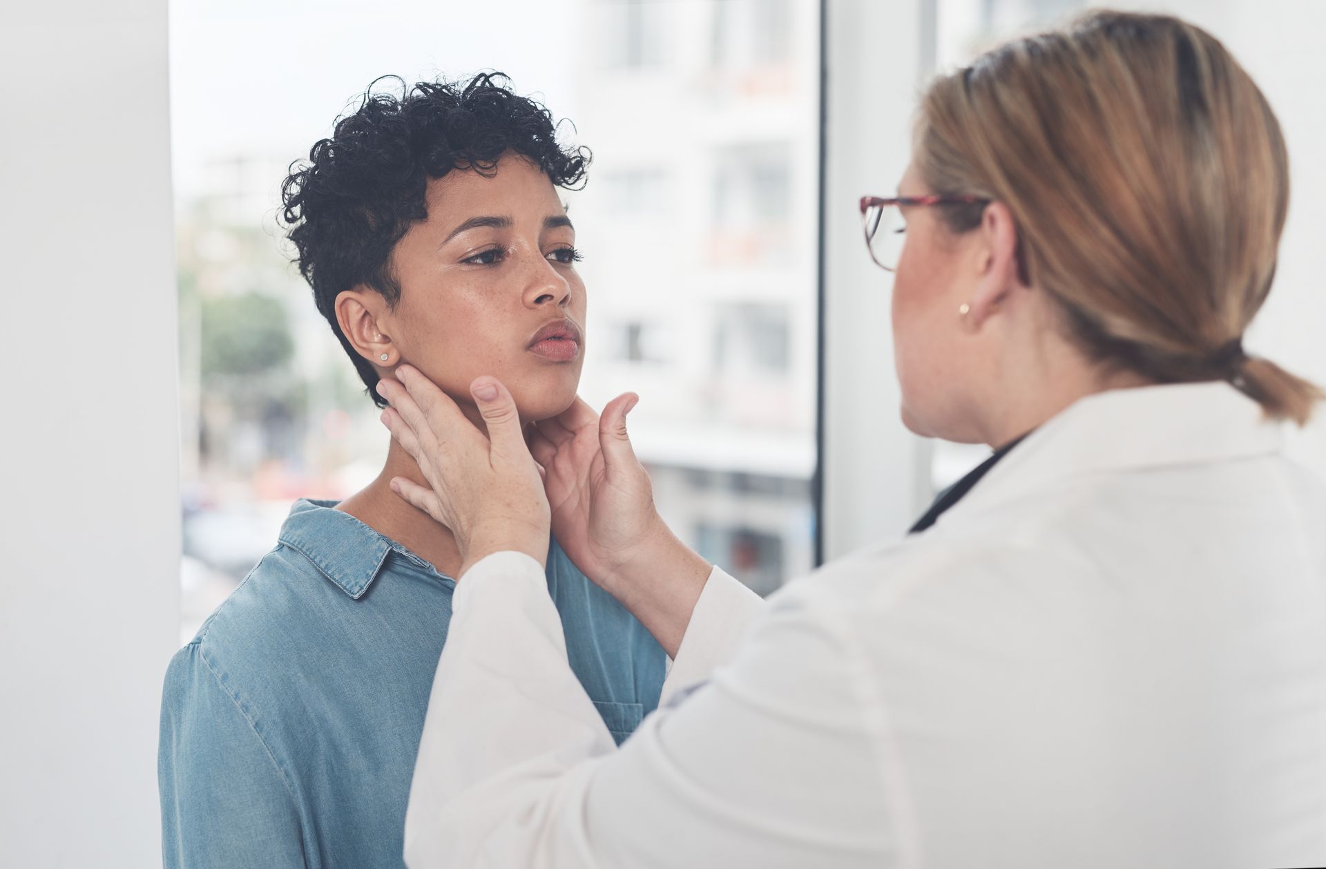 Doctor examining a patient’s jaw in a bright clinic, with the patient seated and facing her.