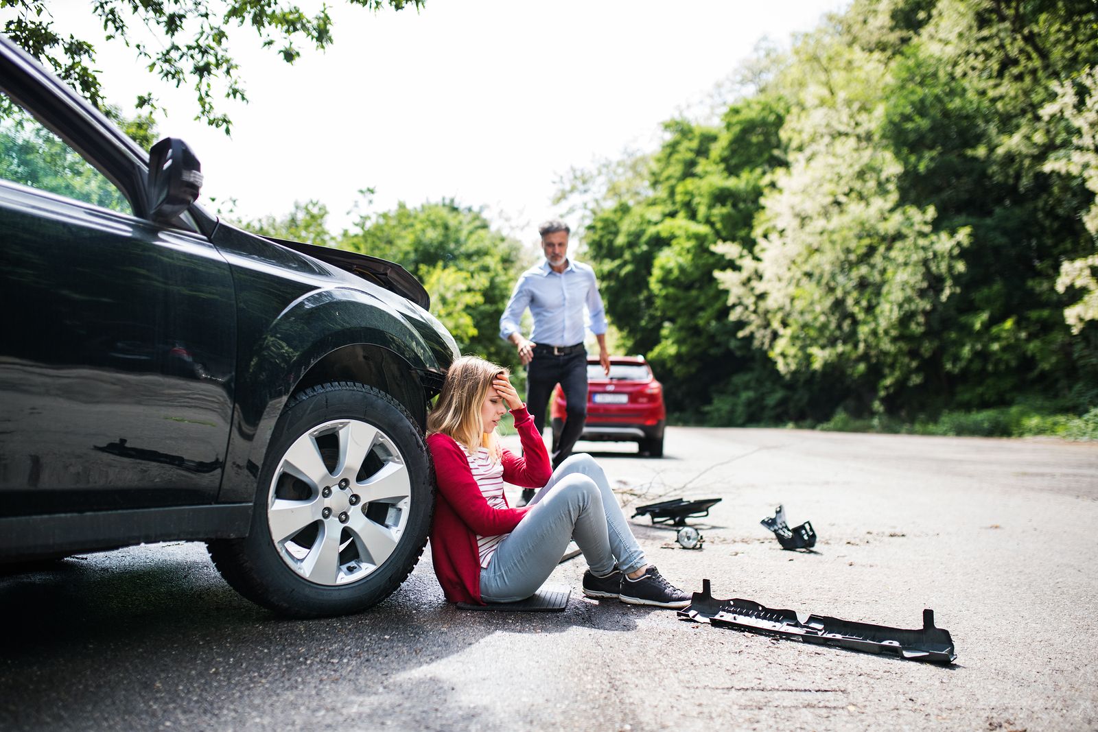 A woman is sitting on the ground next to a car after a car accident.