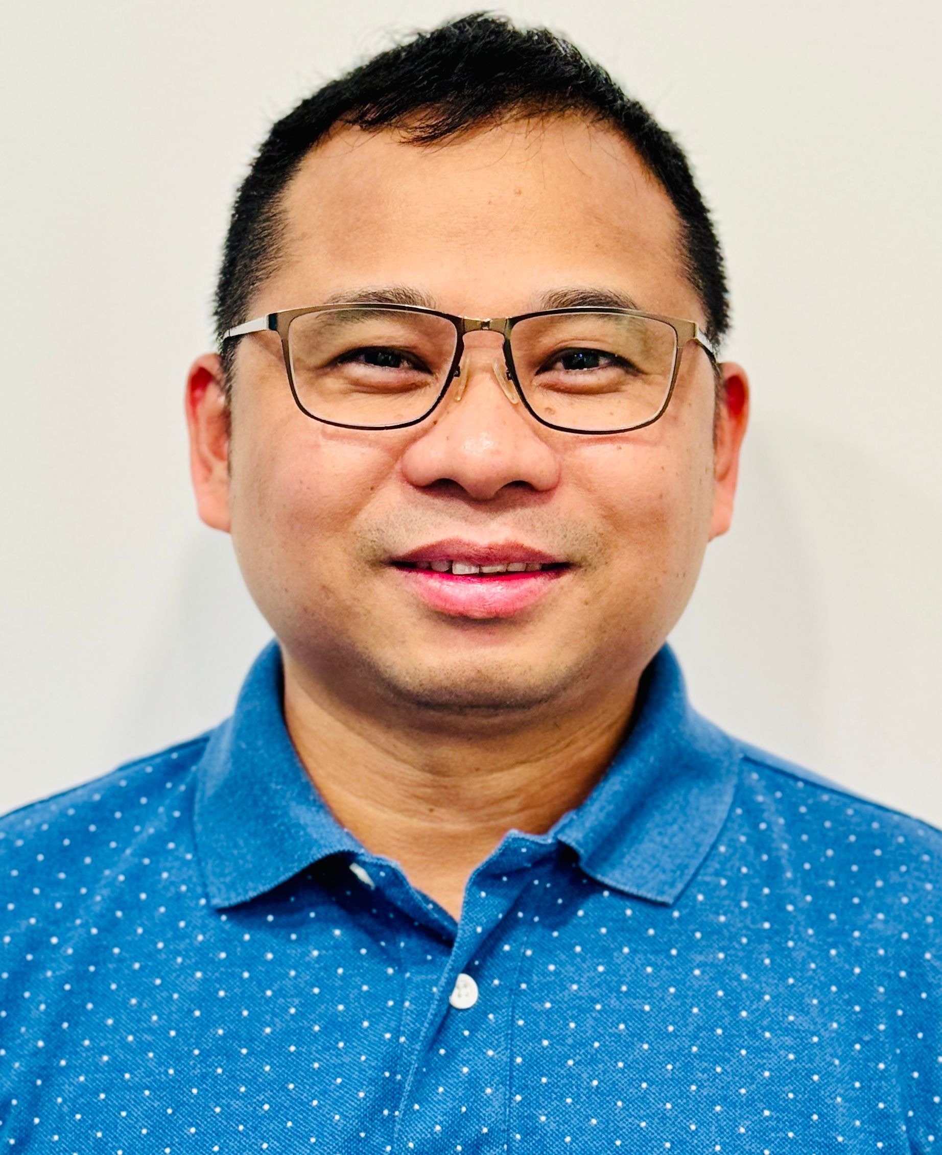 A man wearing glasses and a blue shirt is smiling for the camera.