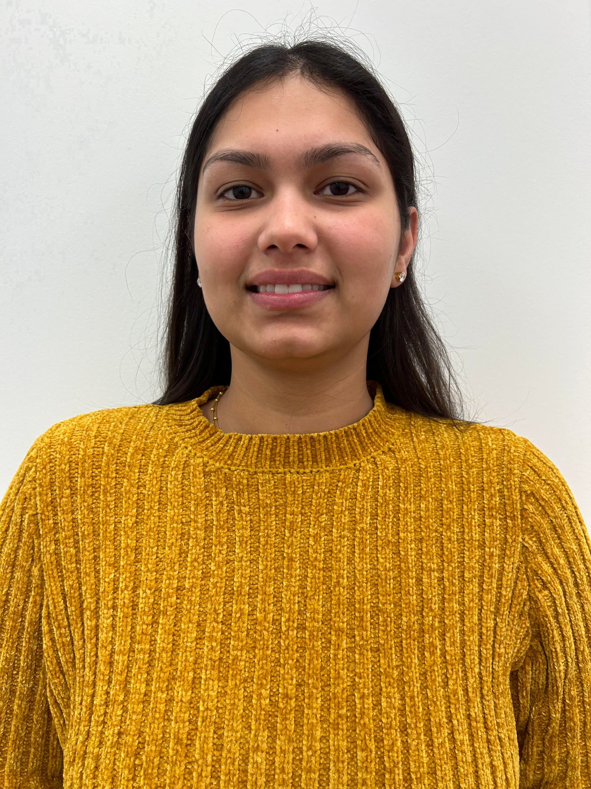 A woman wearing a yellow sweater is smiling for the camera.