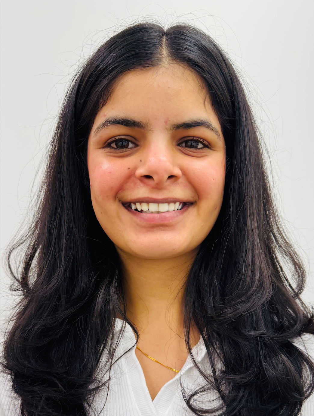 Smiling woman with dark hair, wearing a white shirt, against a white backdrop.