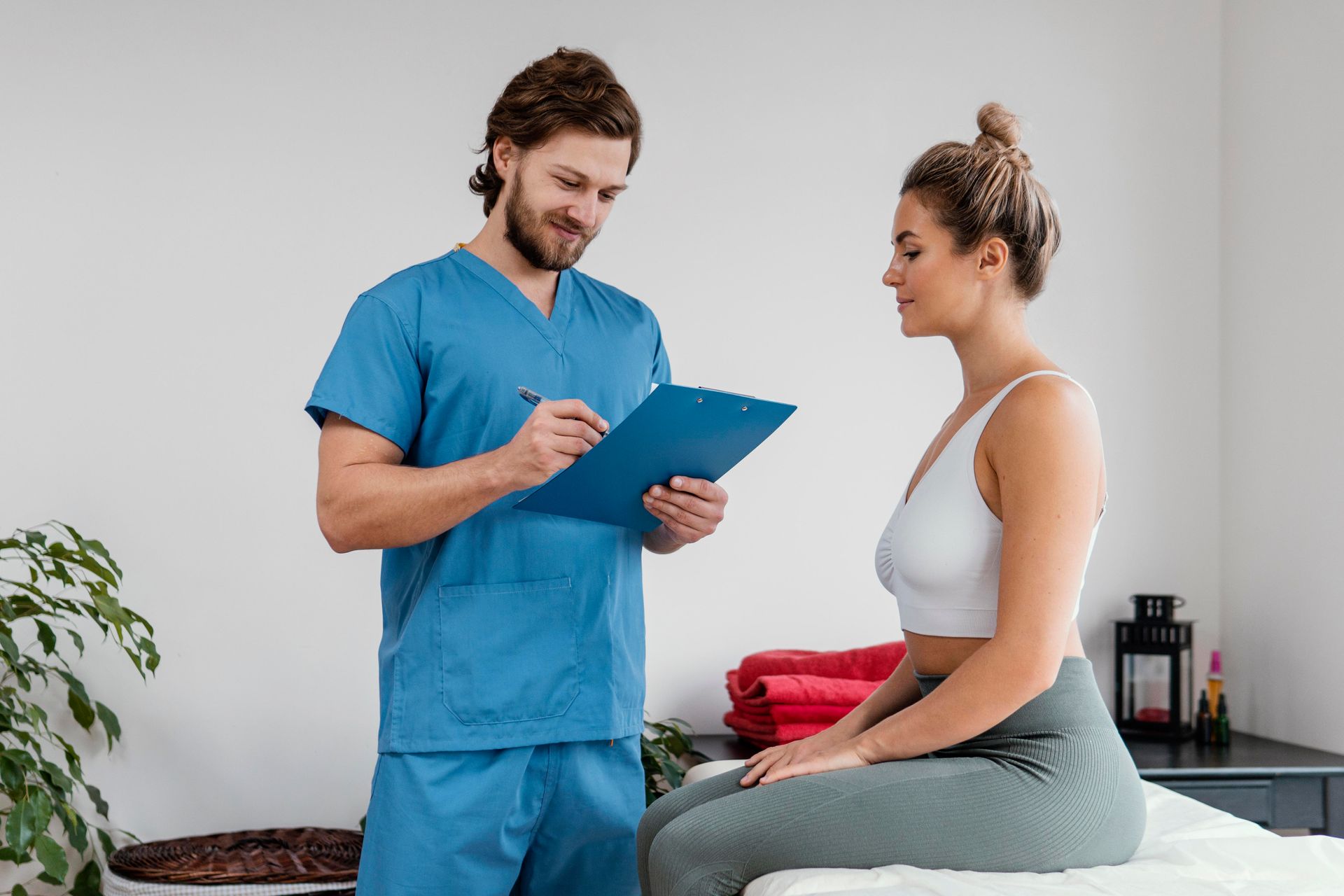 Healthcare provider in blue scrubs consulting a seated patient in a clinic room