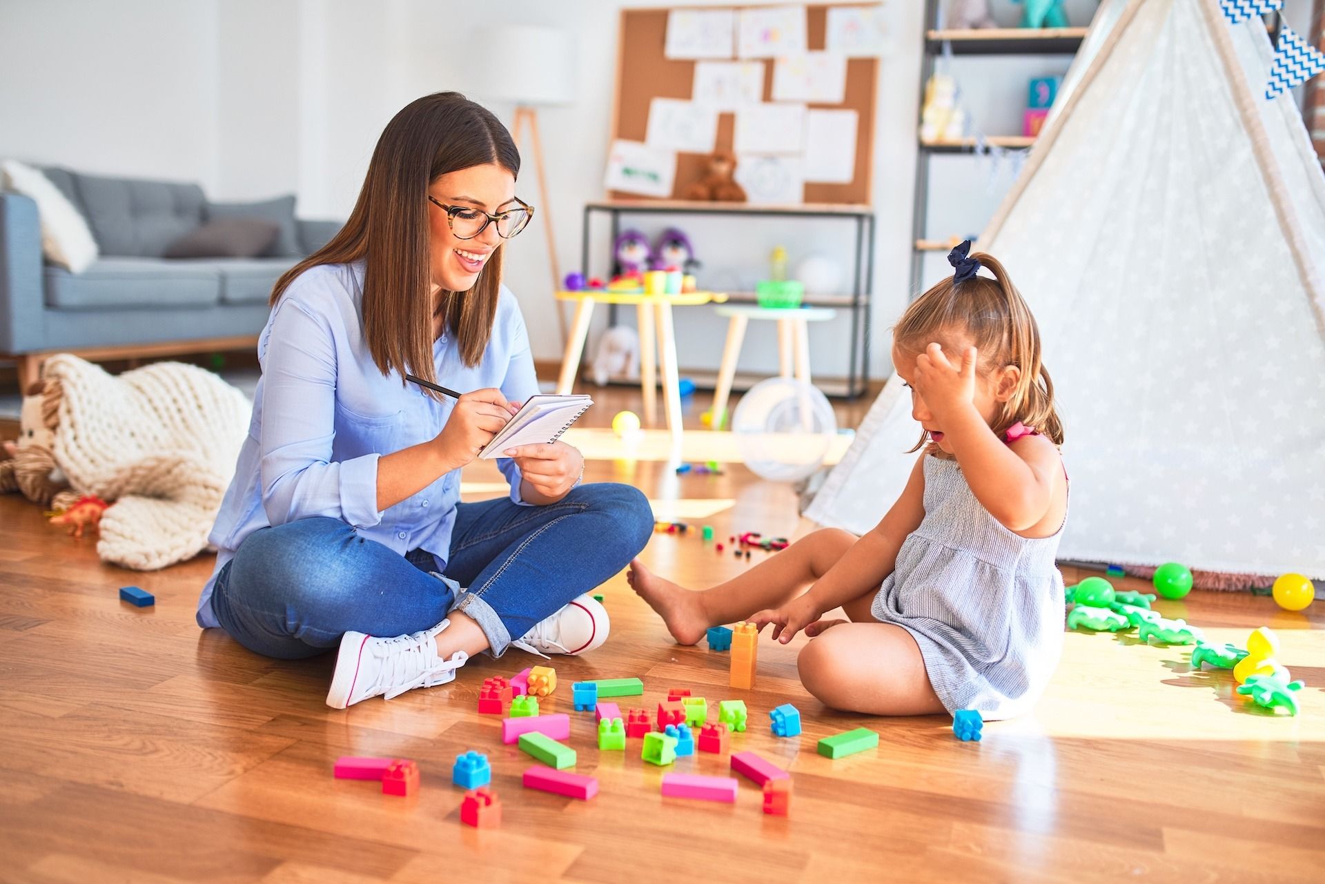 A woman and a little girl are sitting on the floor playing with toys.