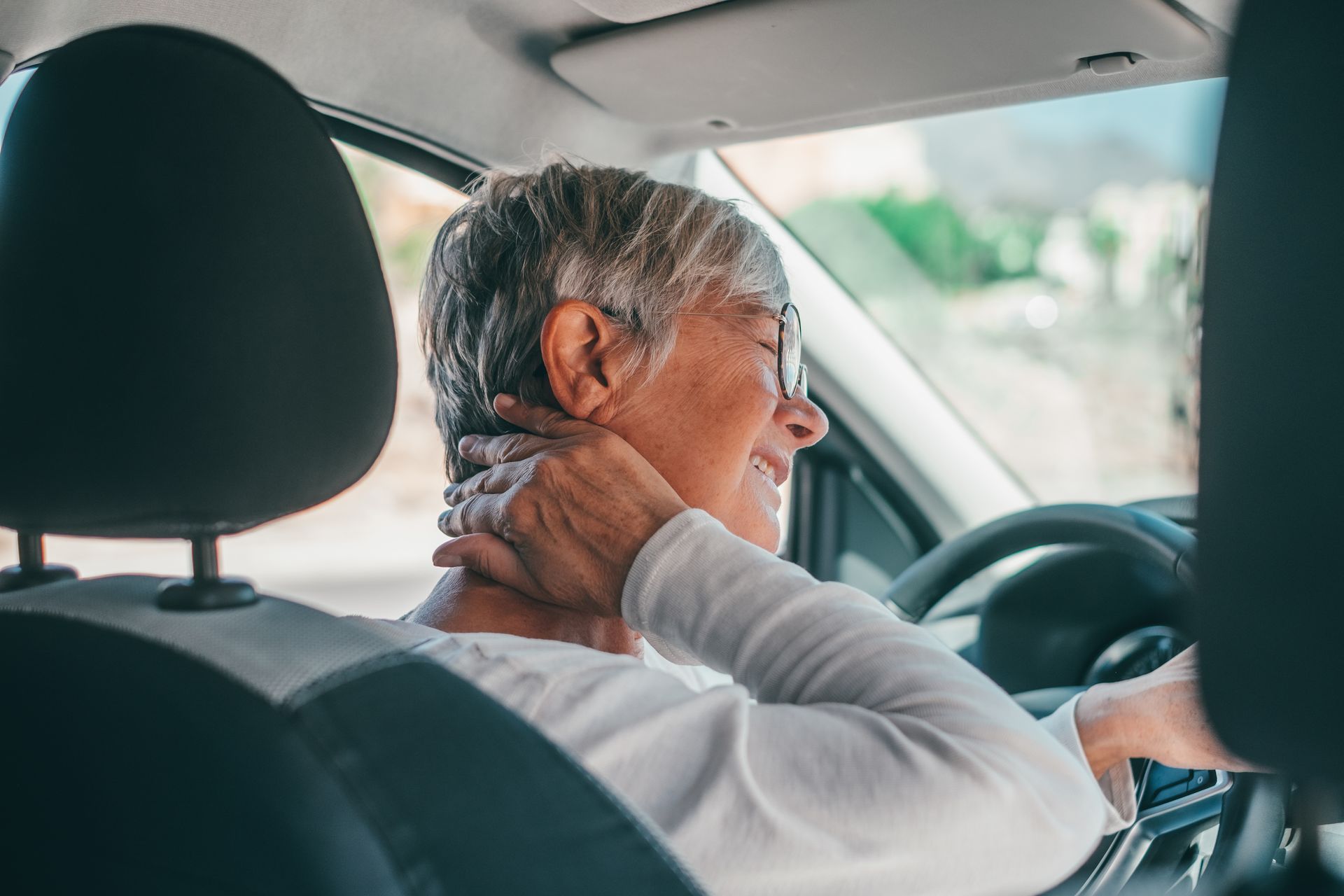 Person driving a car while holding their neck, with a hand on the steering wheel.