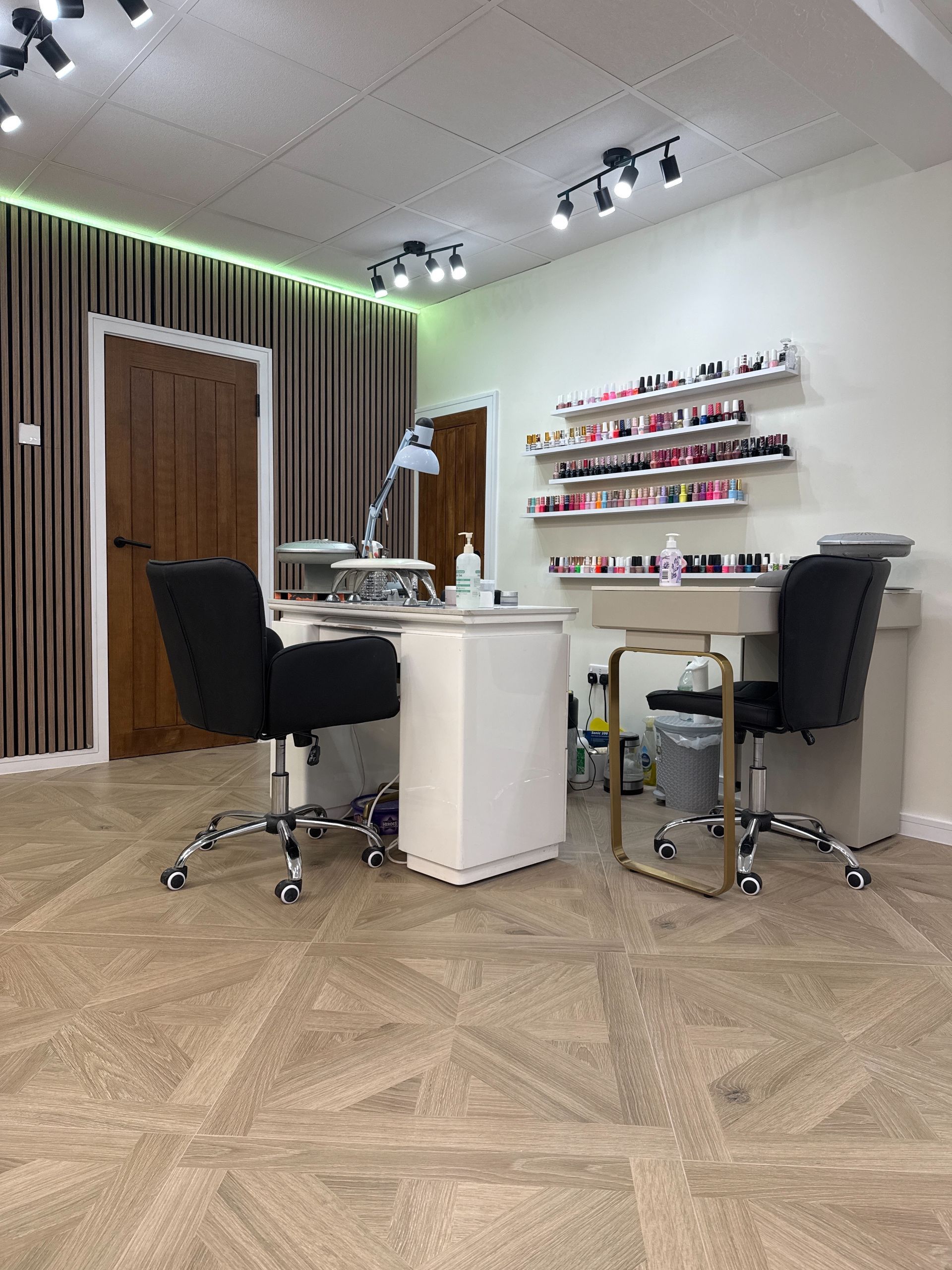 A nail salon with two desks , chairs and shelves of nail polish.