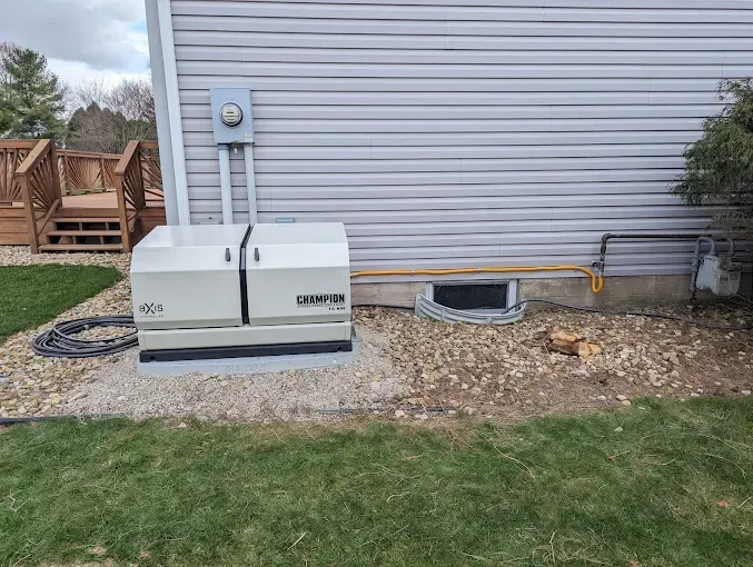 A Generac generator outside a house on a gravel bed. Electrical conduit runs up the wall.