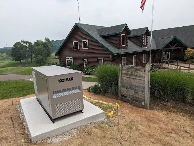Generator on a concrete pad near a log cabin building on a golf course under a cloudy sky.