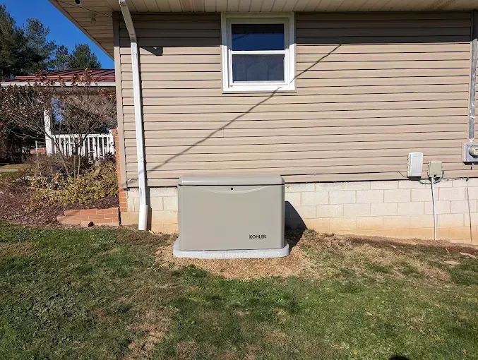 Tan generator next to a house with beige siding, window, and grass.