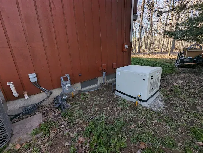 Brown building with a standby generator on a concrete pad. A/C unit and gas meter are visible.