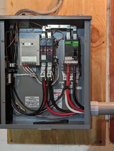 Electrical panel with wires and circuit breakers mounted on plywood.
