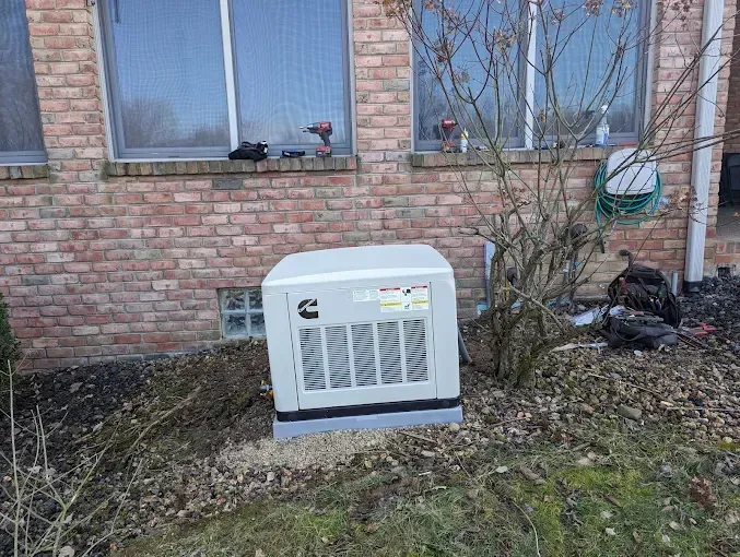 Generator box outside a brick building, sitting on a concrete pad with foliage around it.