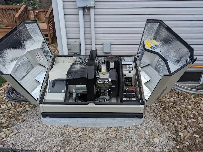Generator with open insulated covers, on a concrete base, next to a house.