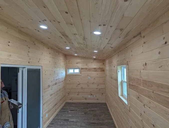 Interior of a small room with wood walls and ceiling, recessed lights, and small windows.