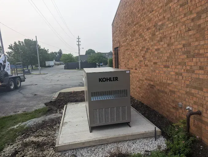 A Kohler generator on a concrete pad next to a brick building.