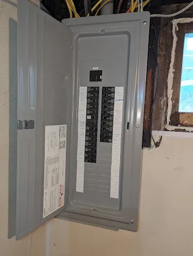 Open electrical panel with circuit breakers. Grey metal box on a beige wall.
