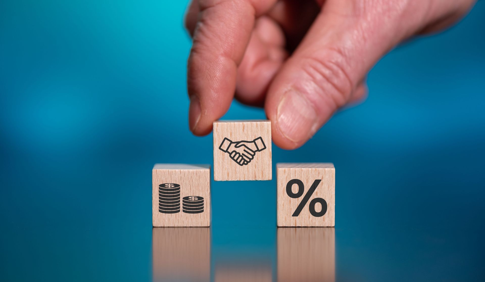 Hand arranging blocks with money, handshake, and percent symbols.