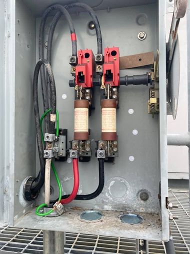 Open electrical panel with red and black wiring, fuses, and gray enclosure interior