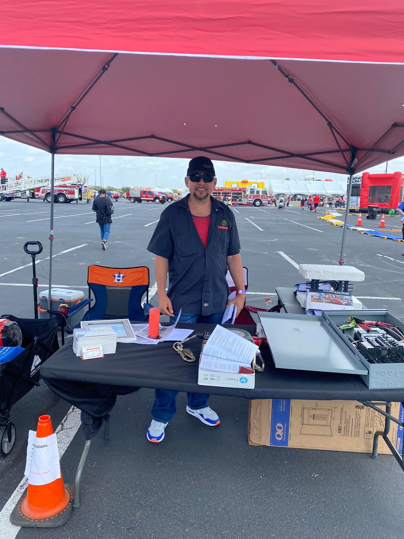 Person behind a table under a pink canopy at an outdoor event, with papers, supplies, and orange cones.