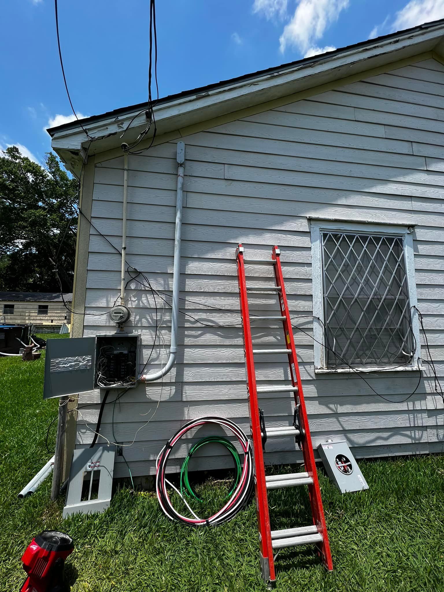 Side of a house with two red ladders, coiled hose, and utility boxes in the yard