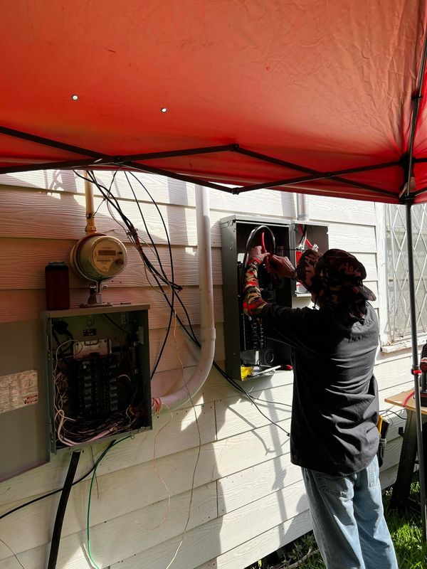 Person hanging decorations under a red canopy beside a house wall and electrical box