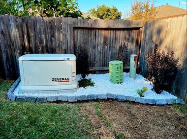 Outdoor Generac generator on a concrete pad beside a wooden fence, with a green utility box and post.