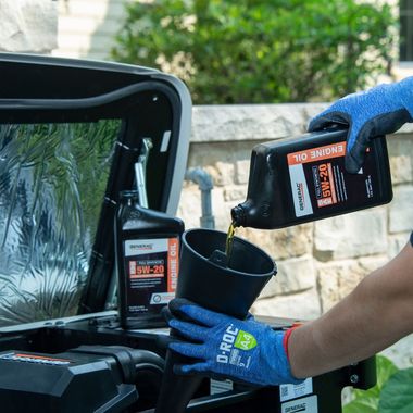 Gloved hands pour black liquid from a jug into a cup beside a car trunk.