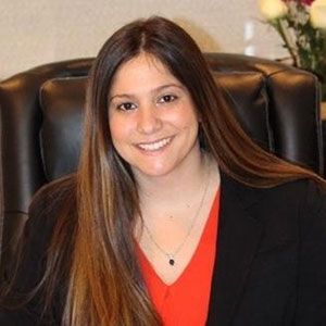 A woman is sitting in a chair wearing a red shirt and a black jacket.