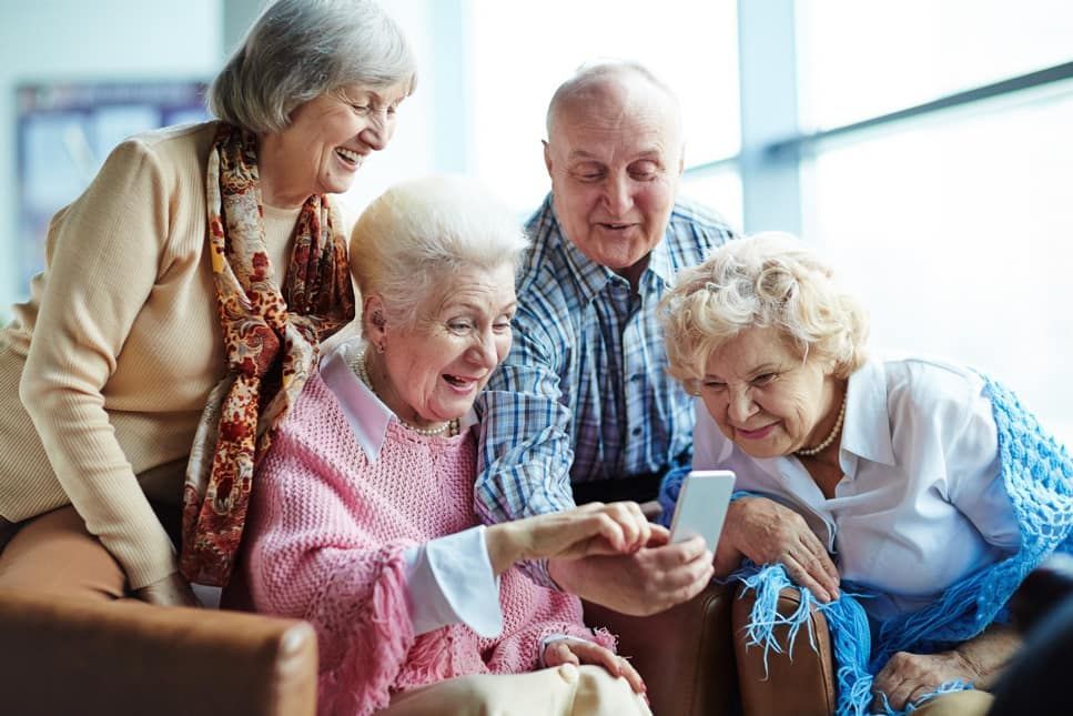 A group of elderly people are sitting on a couch looking at a cell phone.