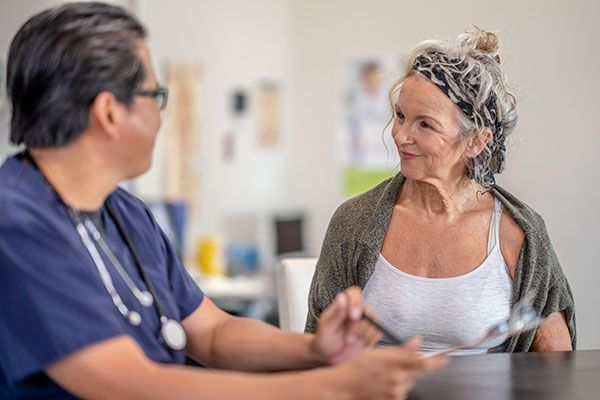 An older woman is sitting at a table talking to a doctor.