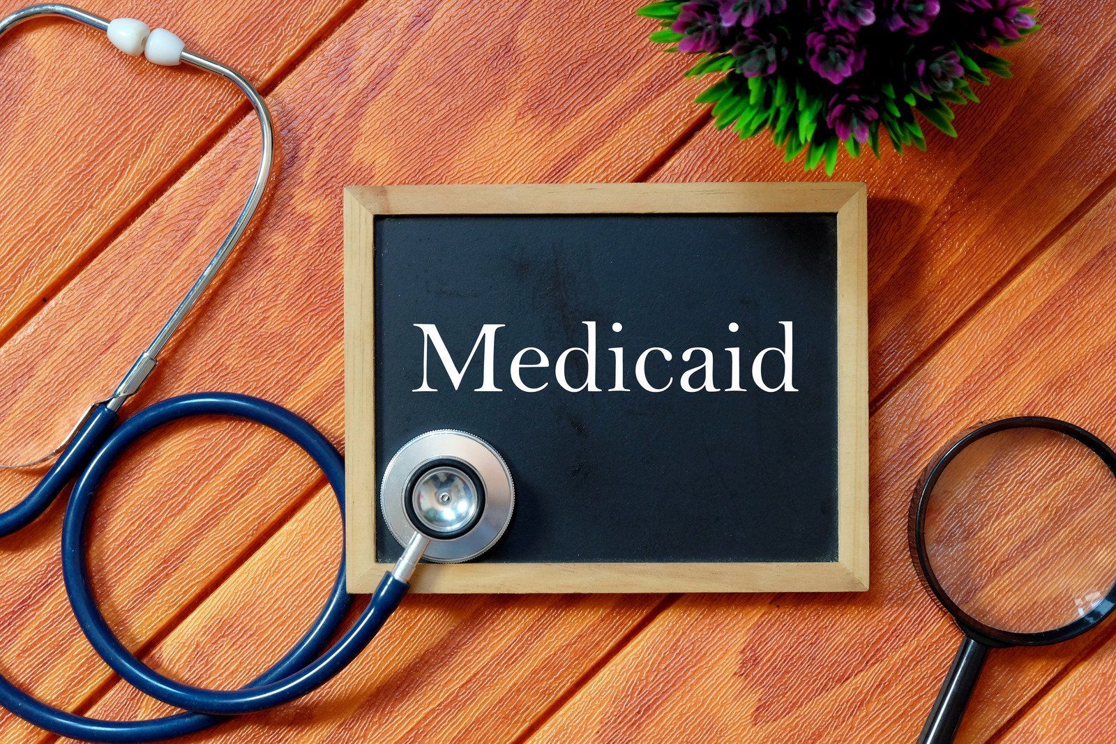 A blackboard with the word medicaid written on it next to a stethoscope and magnifying glass.