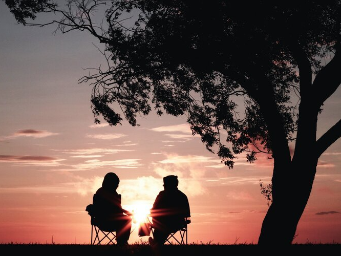 Two people sitting under a tree at sunset