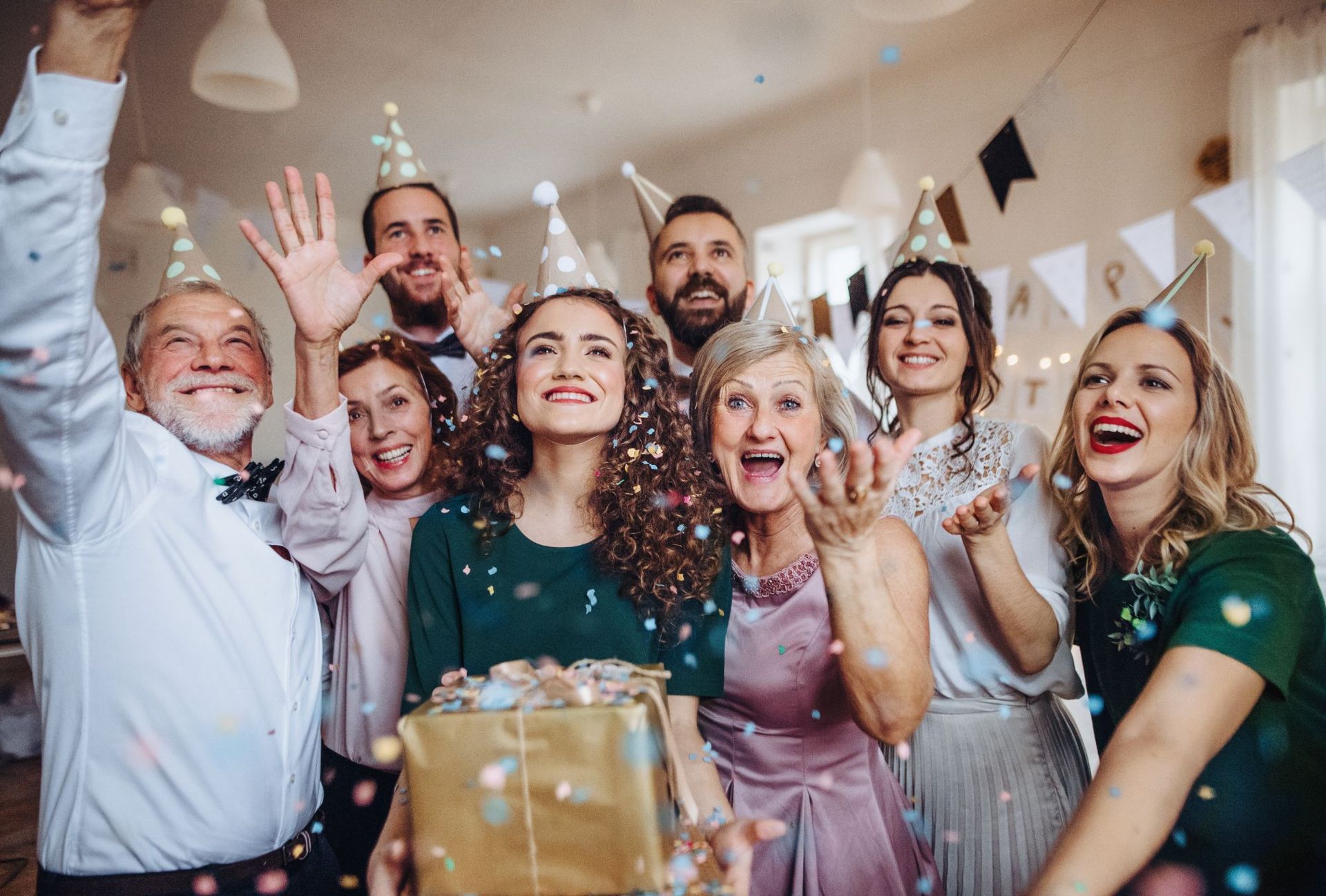 A group of people are standing around a woman holding a gift box at a party.