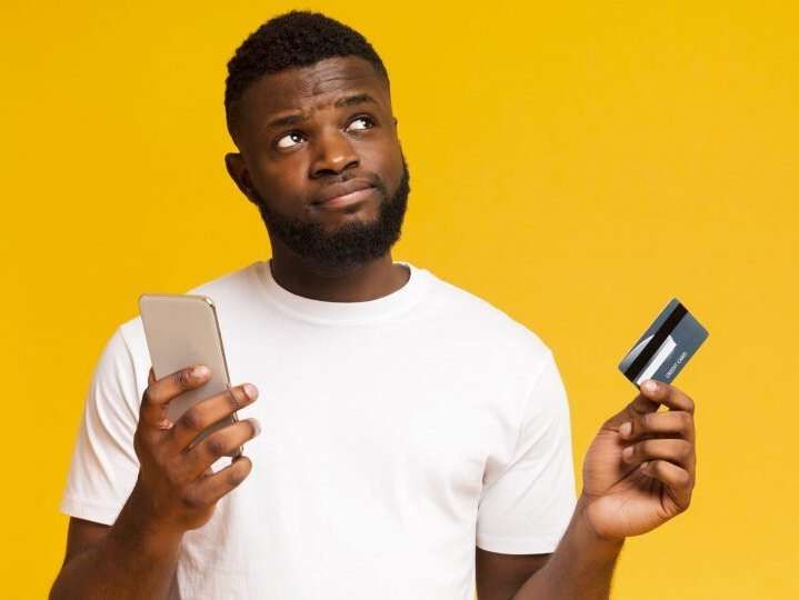 A man is holding a credit card and a cell phone.