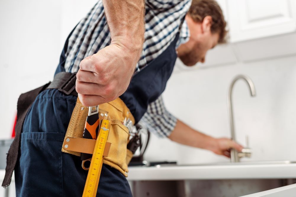 A man is measuring a faucet in a kitchen.