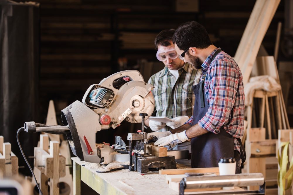 Two men are working on a circular saw in a workshop.