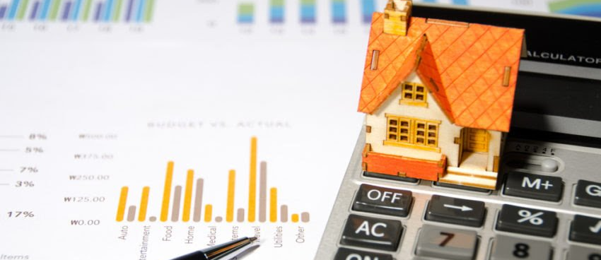 A model house is sitting on top of a calculator next to a pen.