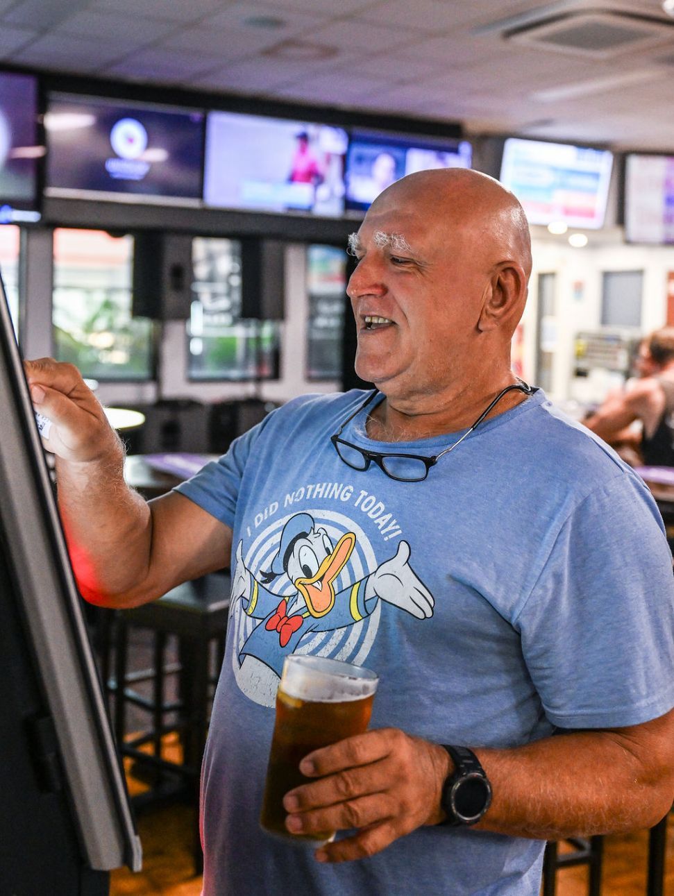 A Man Holding a Beer While Interacting With a Large Monitor — Pub in Stuart Park, NT 