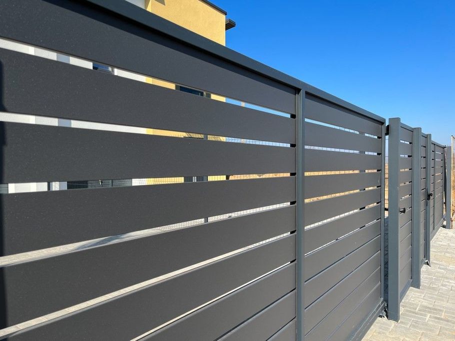 Gray slatted metal fence along a sidewalk under a clear blue sky