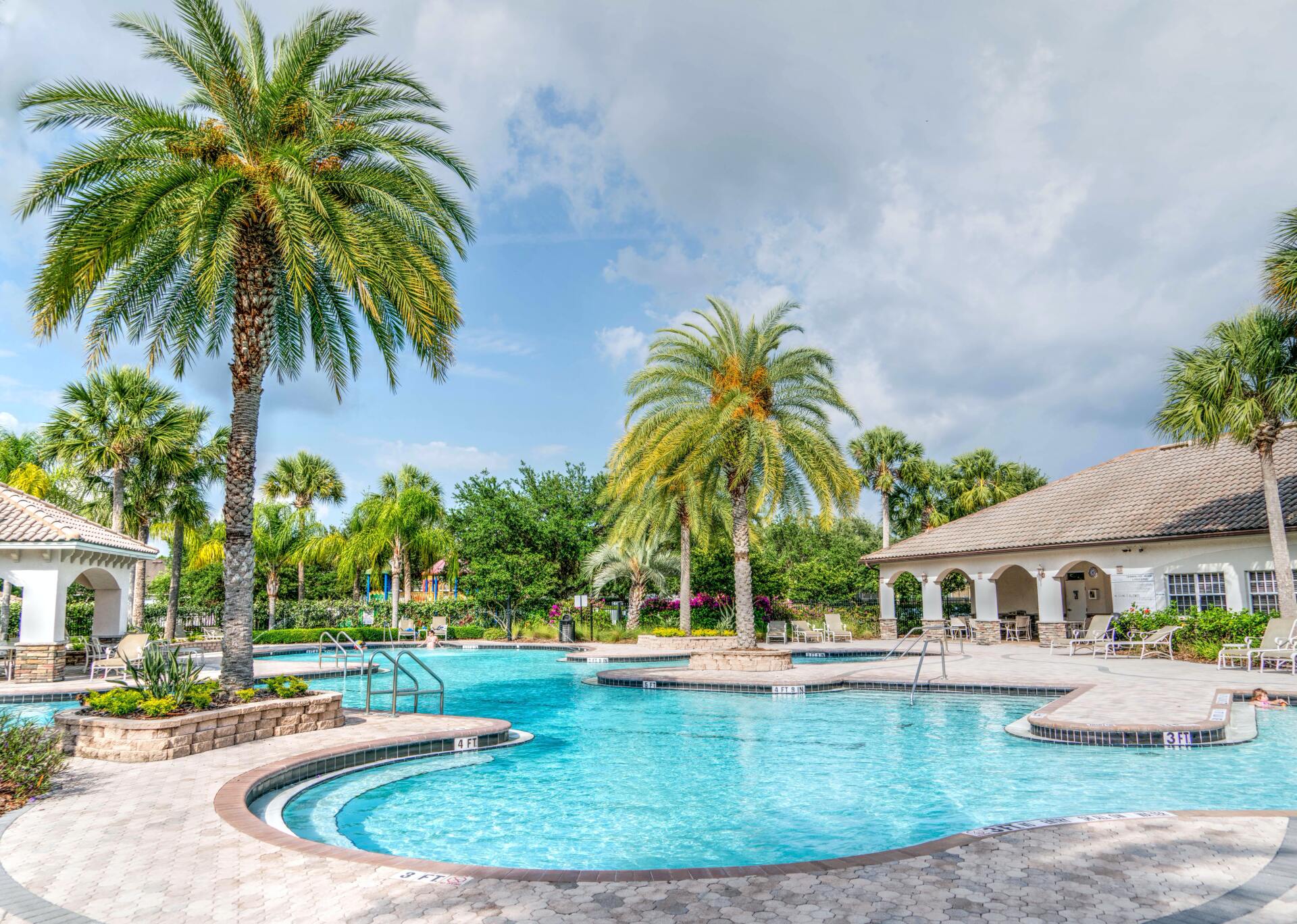 Pool and palm trees at a resort under a cloudy blue sky.