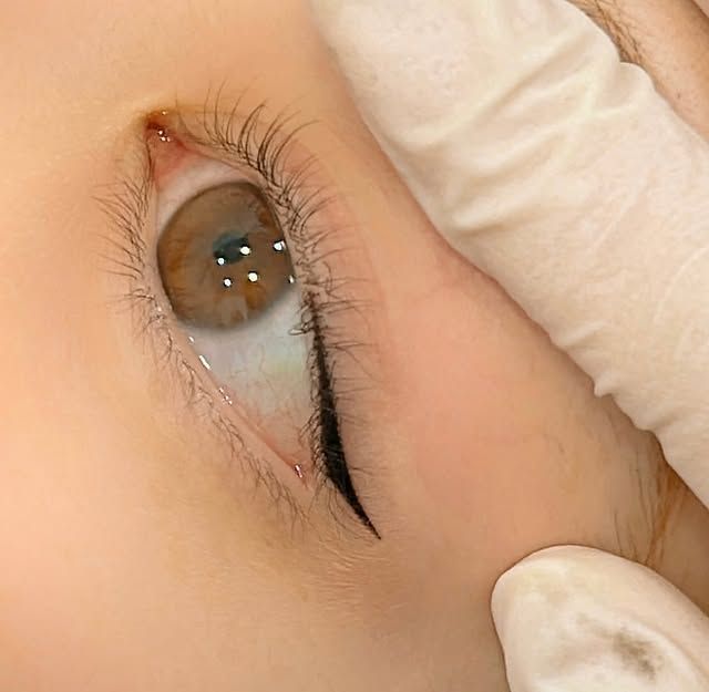 Eye with eyeliner being applied, brown iris, gloved hand.