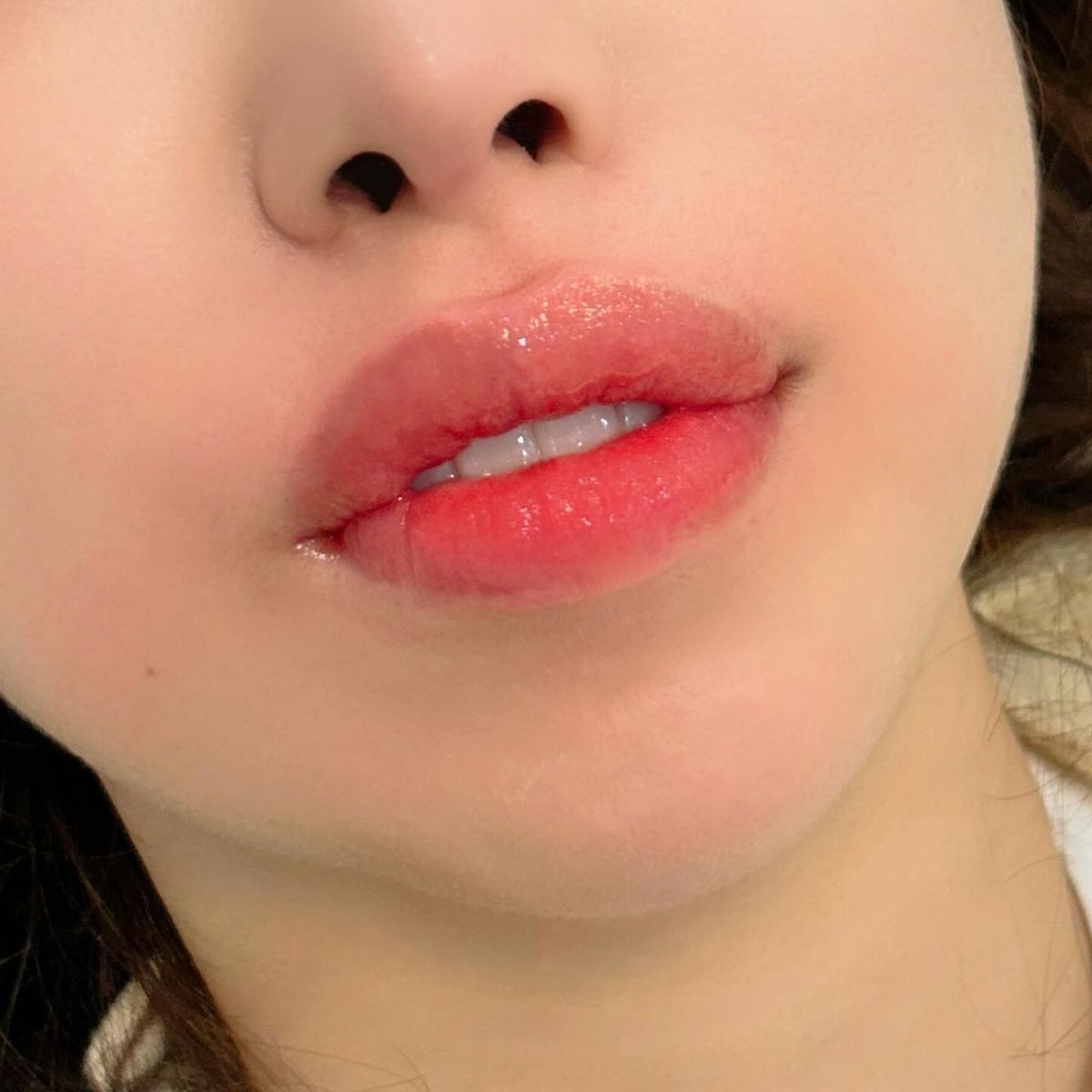 Close-up of a person's glossy lips with red-tinted color. The skin around the mouth is slightly flushed.