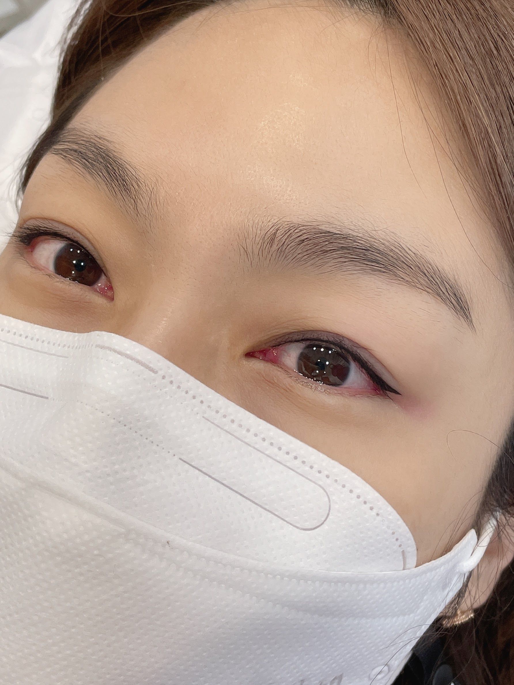 Close-up of a person with neatly shaped, filled-in eyebrows and light brown eyes, partially covered by a white cloth.