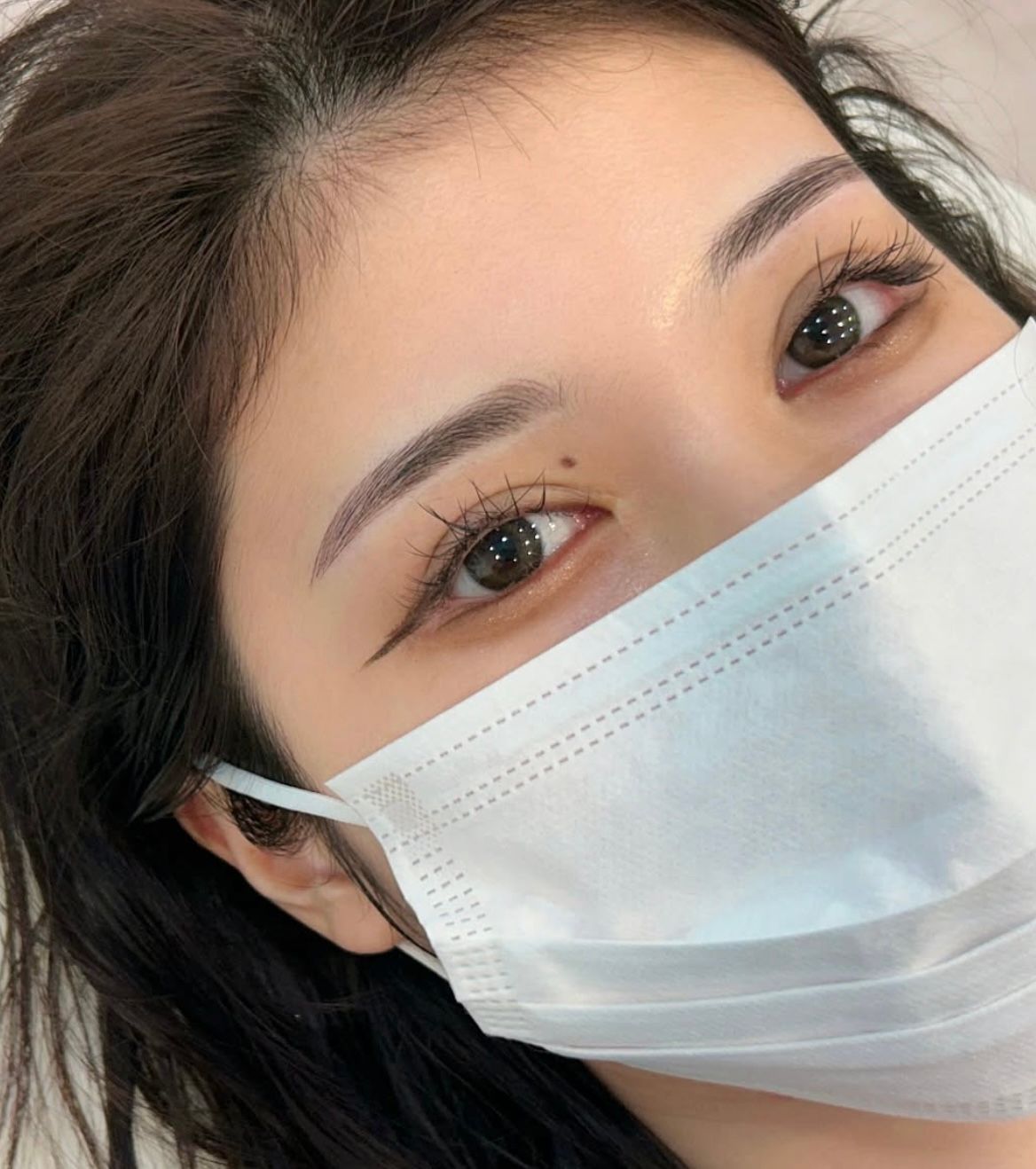 Person wearing a mask; makeup on eyebrows and eyeliner.