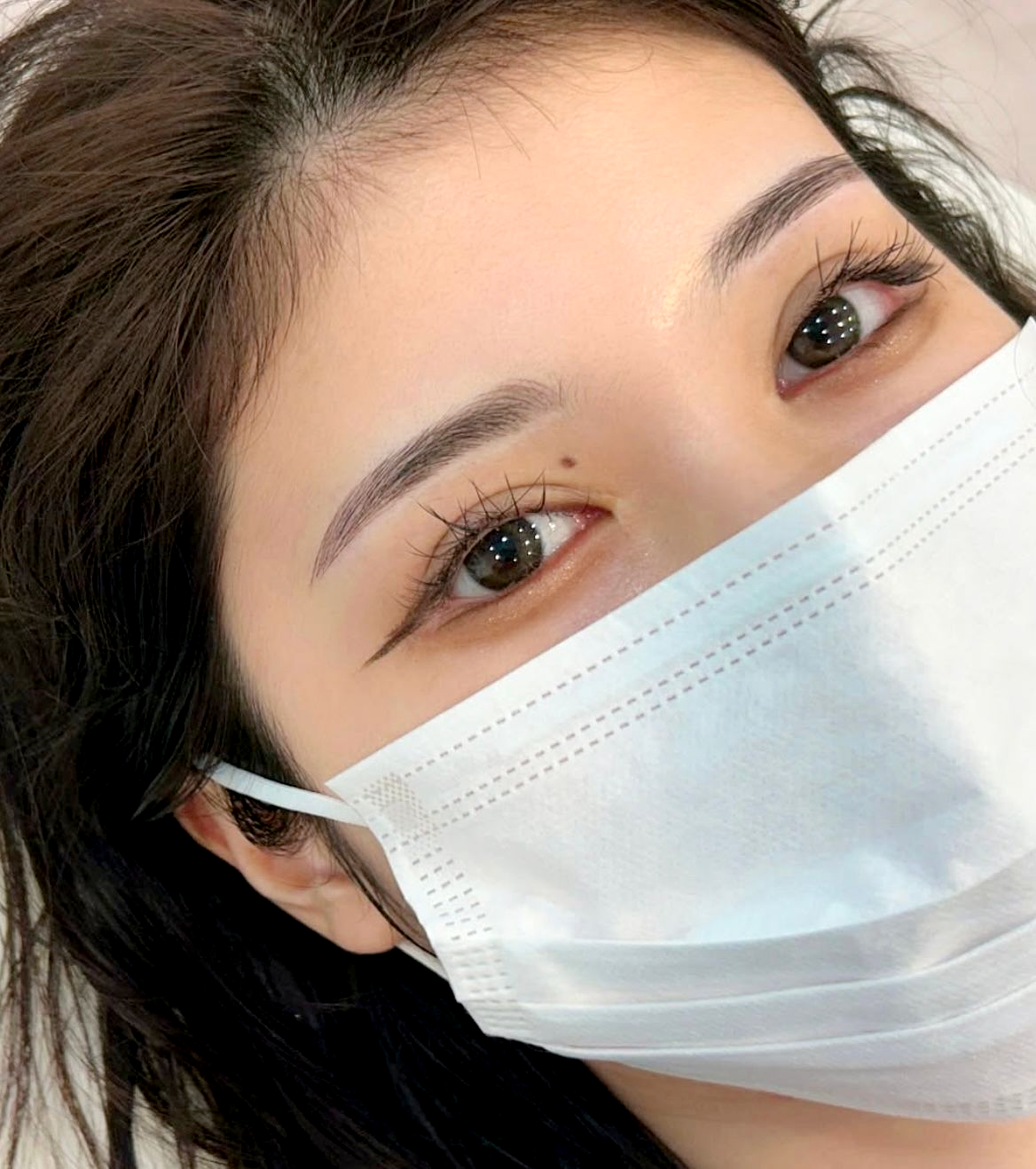 Woman with delicate eyeliner, eyebrows, and a face mask; brown eyes.