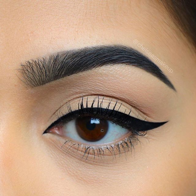Close-up of eye with black winged eyeliner, full eyebrow, and neutral eyeshadow. Brown eye.