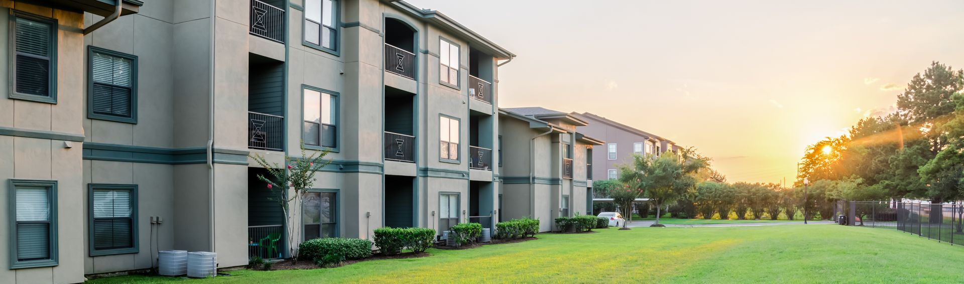 Apartment complex with balconies beside a green lawn at sunset