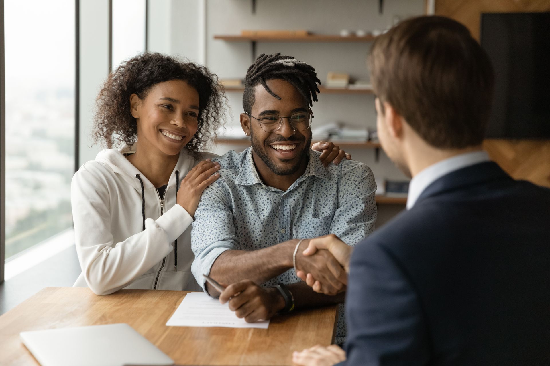Two people smiling during a business meeting across a table with a suited man in an office